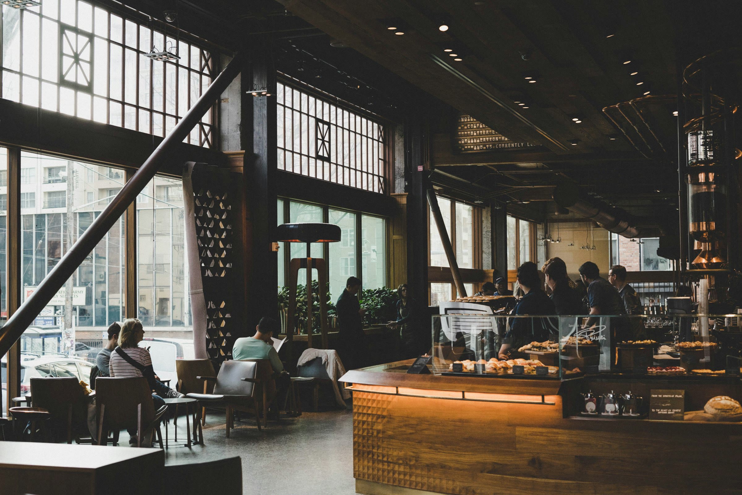 A wide, high-ceilinged hall with a long lit bar and tall steel windows