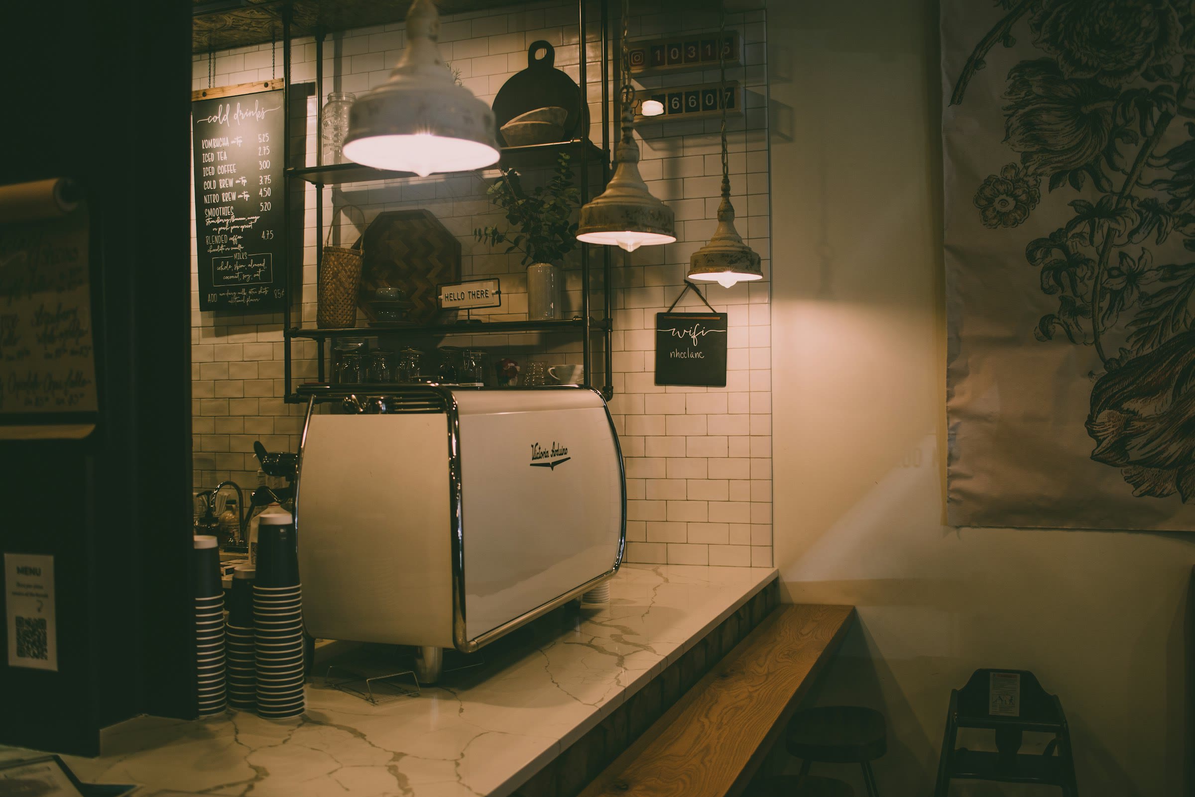 An espresso machine on a pale counter under low hanging lamps