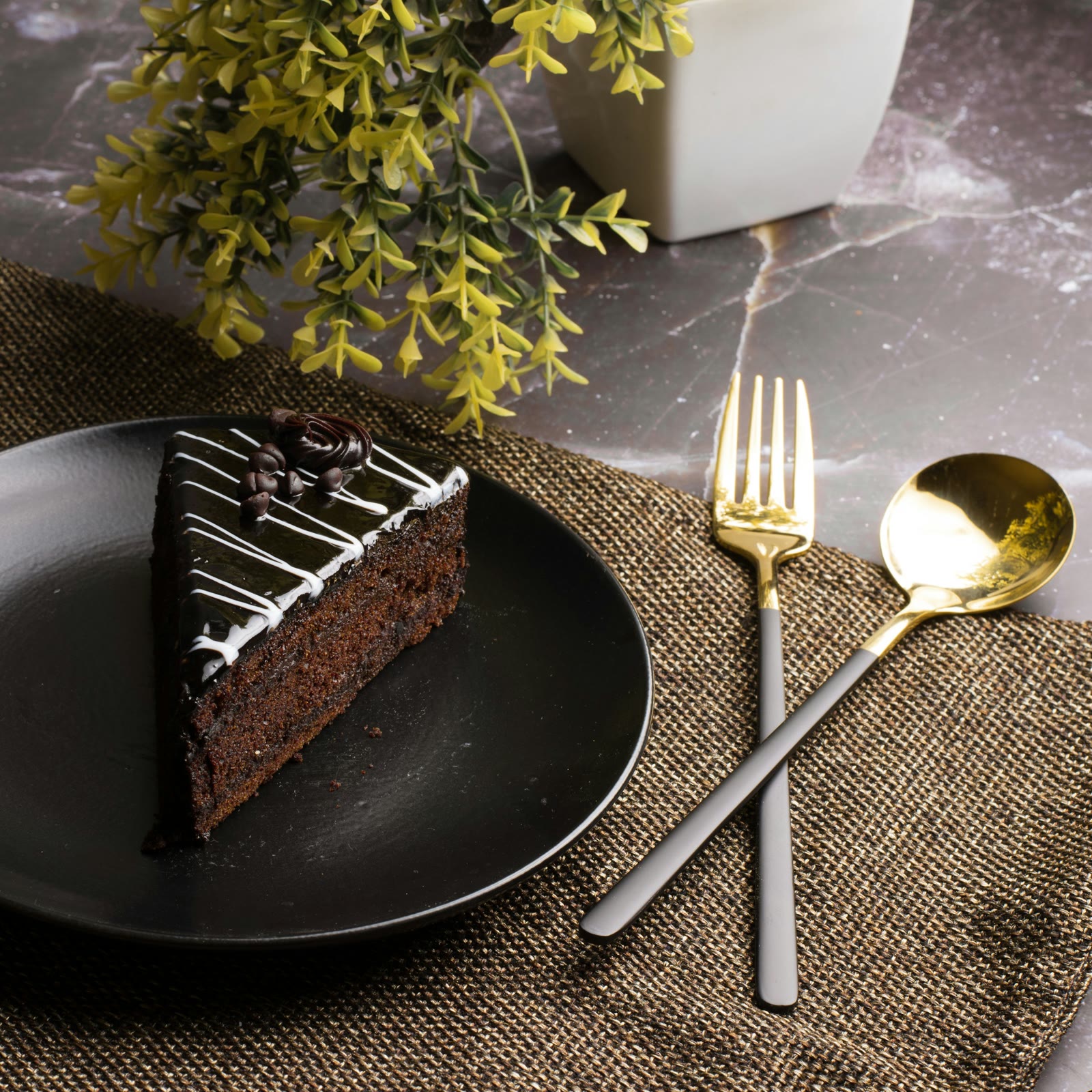 A slice of layered chocolate cake on a black plate with brass cutlery