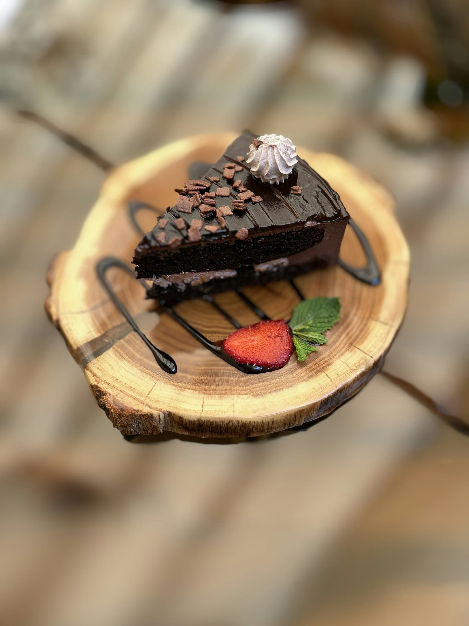 A slice of chocolate cake on a wooden round with a strawberry