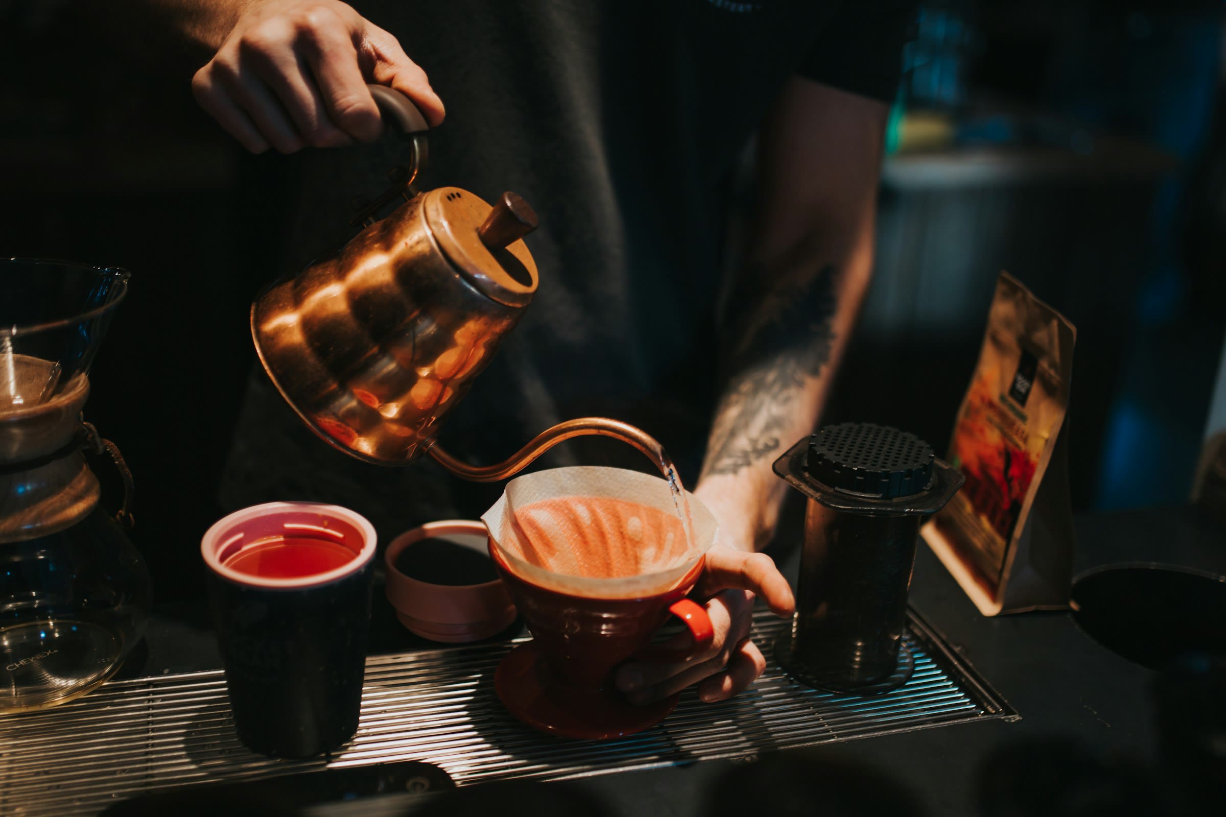 A copper kettle pouring into a ceramic dripper beside small cups