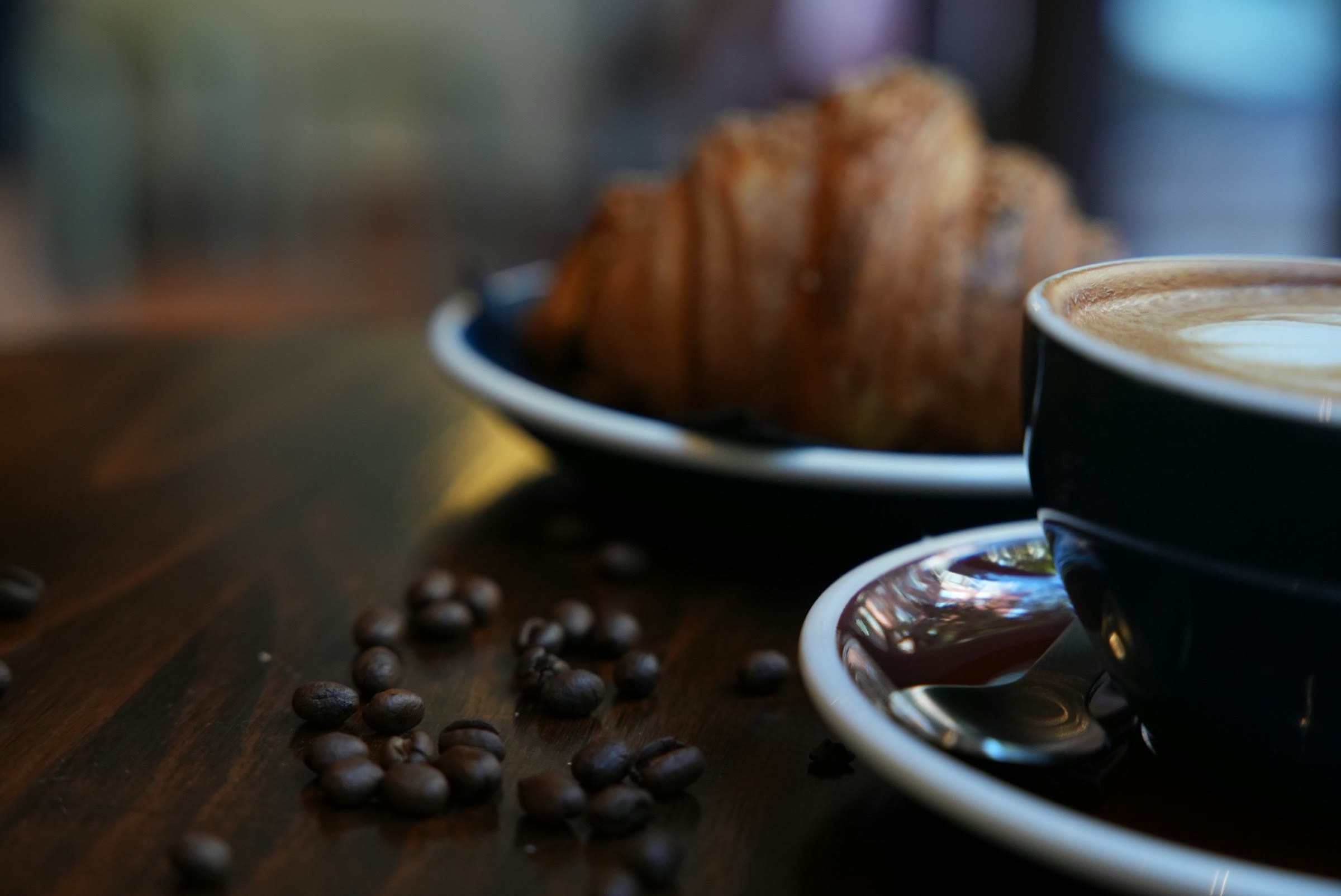 A croissant and a cup of coffee on a dark wooden table