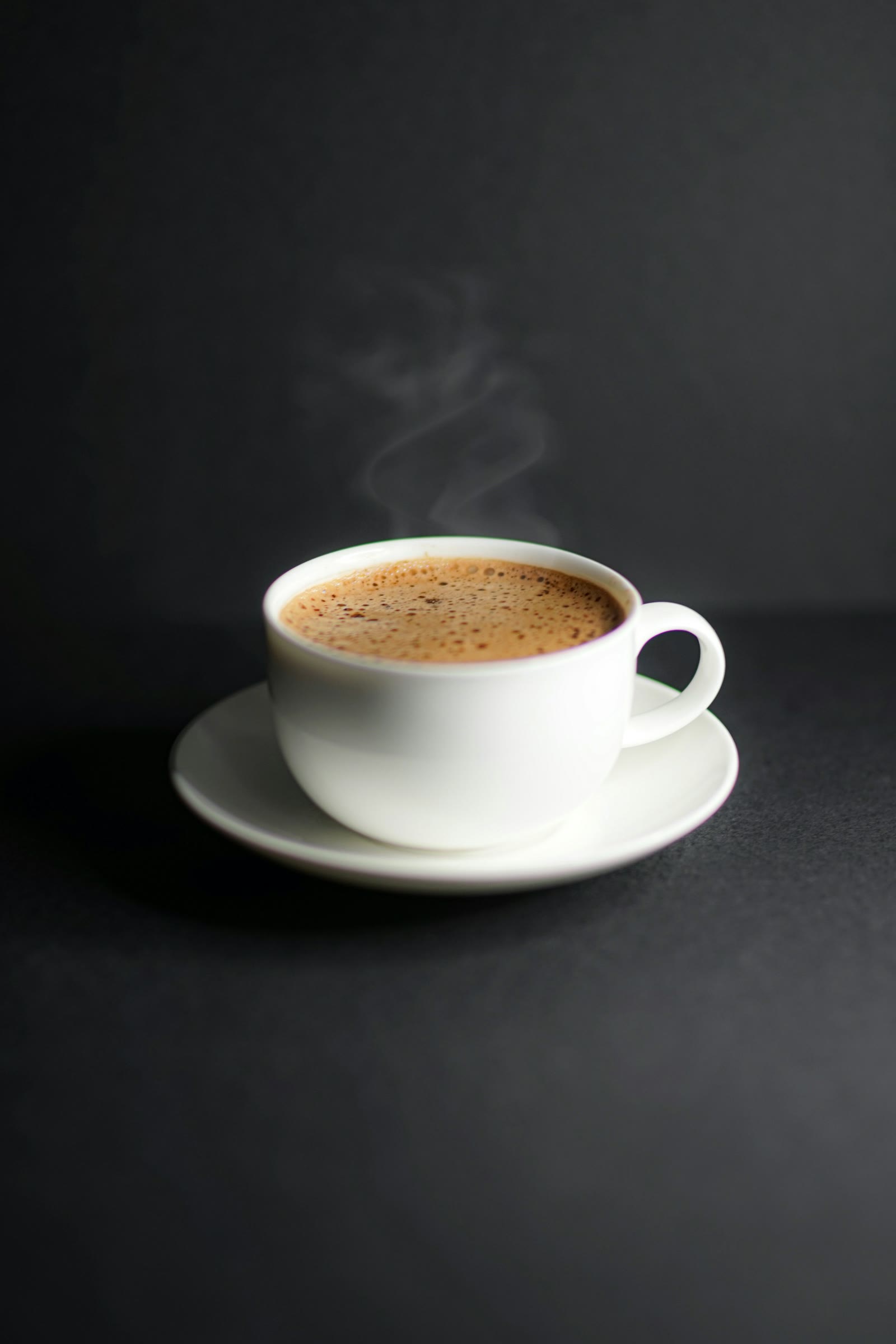 A white cup and saucer with a thin curl of steam on a dark table