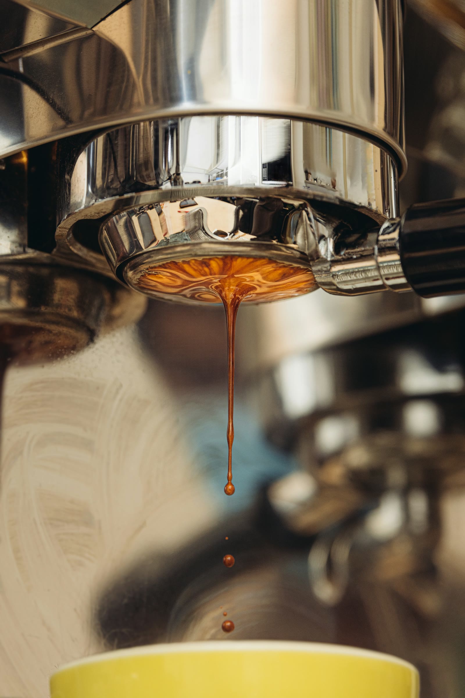 A thin stream of espresso falling from a chrome portafilter