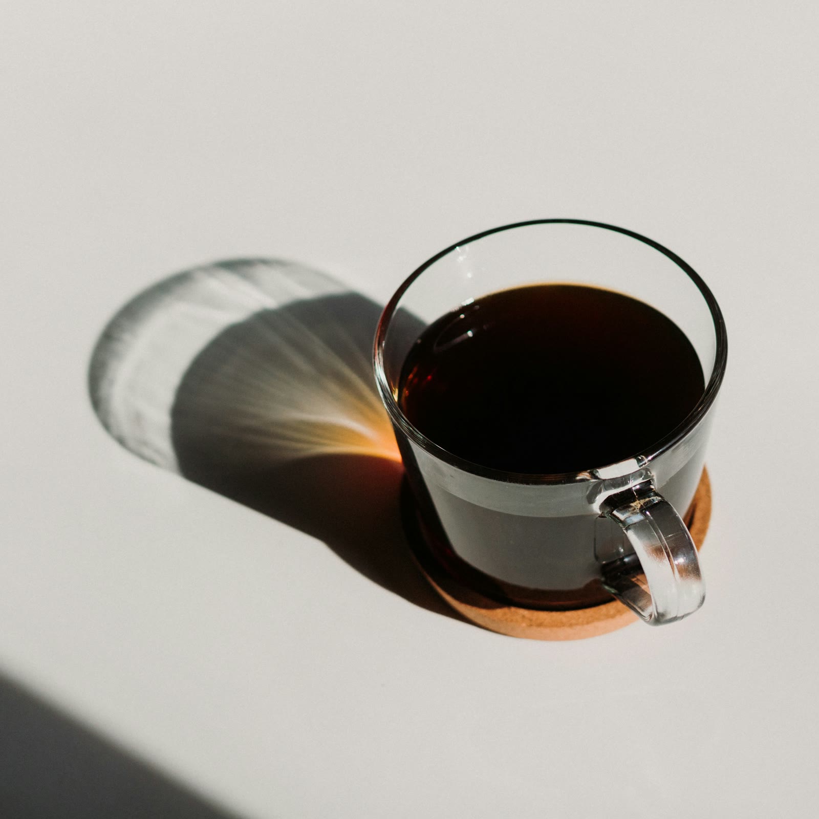 A glass mug of black coffee throwing a long amber shadow in bright sun