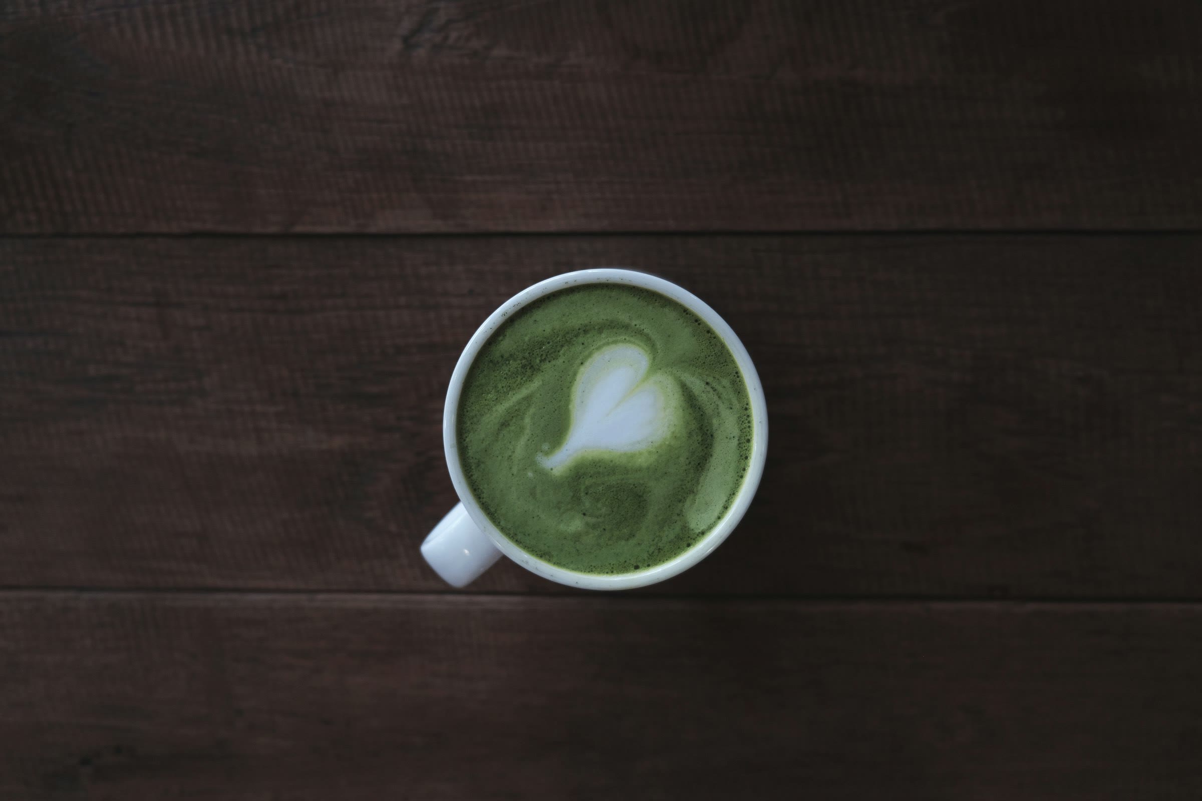 A matcha latte with a heart, seen from above on dark timber